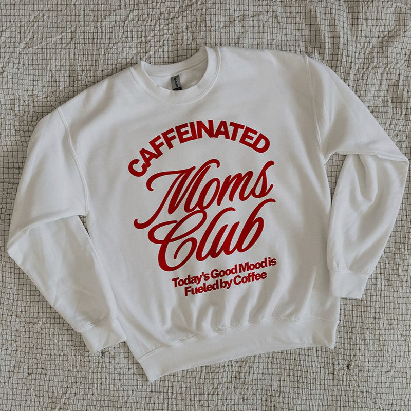 White Caffeinated Moms Club sweatshirt folded neatly on a cozy bed, showing red retro lettering for coffee-loving moms.