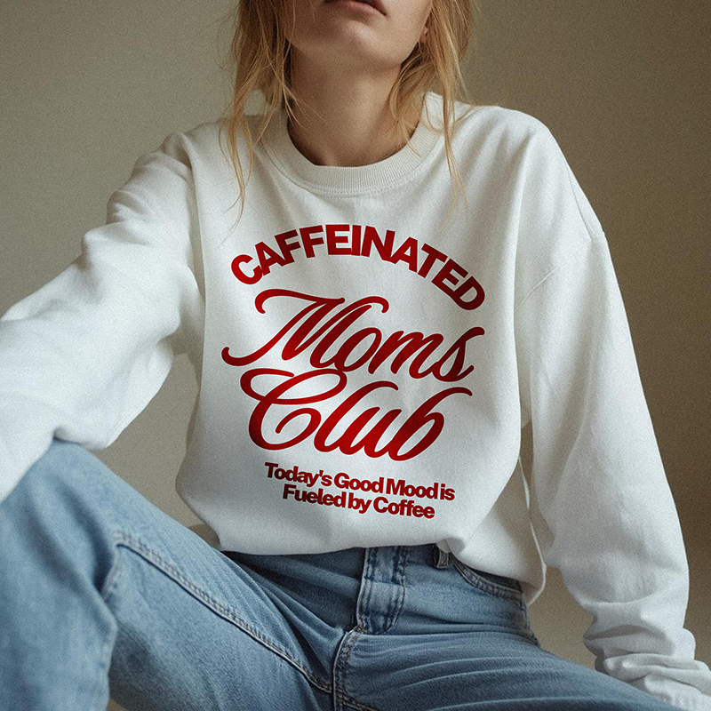 Mom wearing white Caffeinated Moms Club crewneck sweatshirt with red print, styled casually with jeans for a cozy, caffeine-fueled morning look.