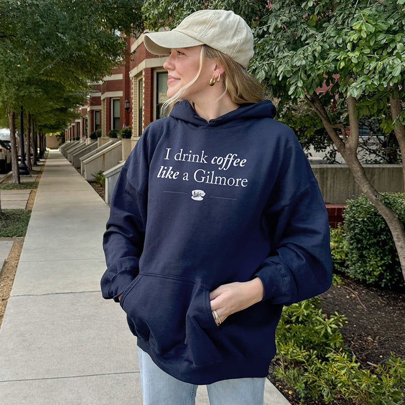 Model wearing navy “I Drink Coffee Like a Gilmore” hoodie outside with hat and jeans – casual coffee lover outfit