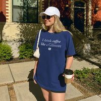 Woman holding coffee wearing I Drink Coffee Like A Gilmore tee in true navy with white hat, cozy Gilmore Girls inspired shirt