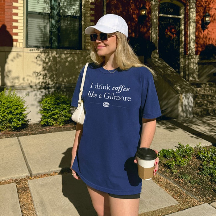 Woman holding coffee wearing I Drink Coffee Like A Gilmore tee in true navy with white hat, cozy Gilmore Girls inspired shirt