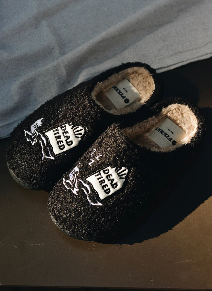 Black fuzzy slippers with embroidered “Dead Tired” design, fleece lining, and rubber sole; cozy unisex loungewear perfect for Halloween or everyday exhaustion.