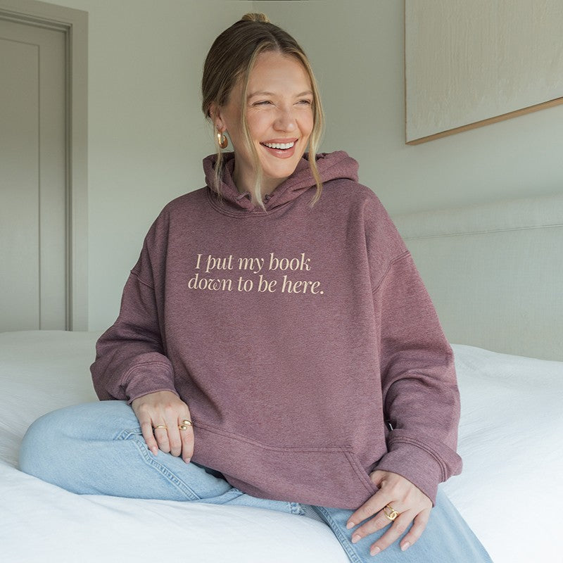Woman wearing heather dark maroon “I Put My Book Down To Be Here” hoodie – cozy sarcastic hoodie for readers who’d rather be home reading