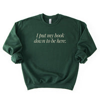 Flatlay of I Put My Book Down To Be Here Sweatshirt in forest green – unisex book lover crewneck.