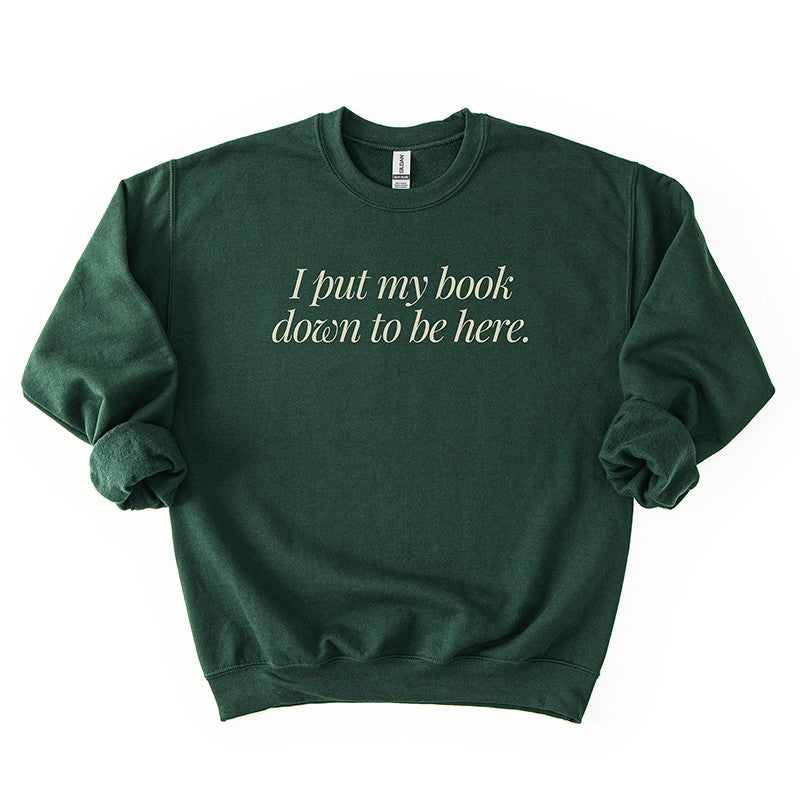 Flatlay of I Put My Book Down To Be Here Sweatshirt in forest green – unisex book lover crewneck.