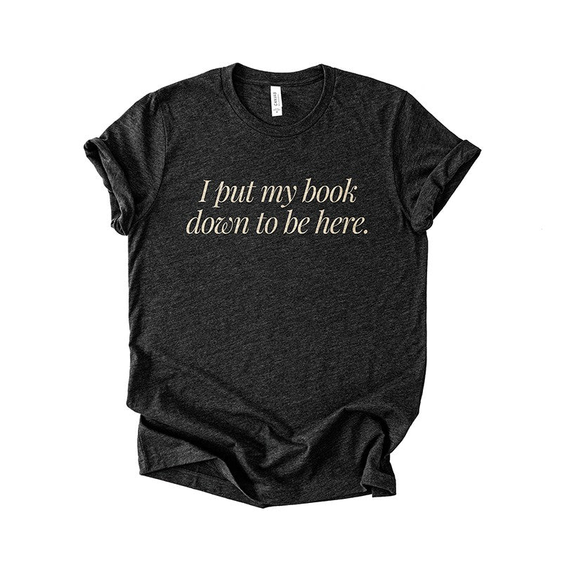 Flatlay of the I Put My Book Down To Be Here Tee in black heather – unisex funny bookish graphic tee.