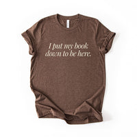 Flatlay of the I Put My Book Down To Be Here Tee in heather brown – bibliophile t-shirt for readers and introverts.