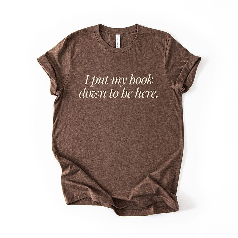 Flatlay of the I Put My Book Down To Be Here Tee in heather brown – bibliophile t-shirt for readers and introverts.