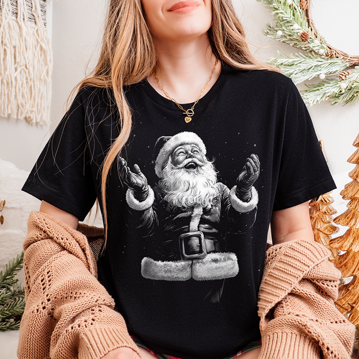 Woman wearing black triblend “Joyful Santa” tee styled with cardigan, festive holiday décor and cozy Christmas setting