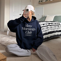 Woman wearing navy Slow Mornings Club hoodie with grey sweatpants for a relaxed coffee lover look