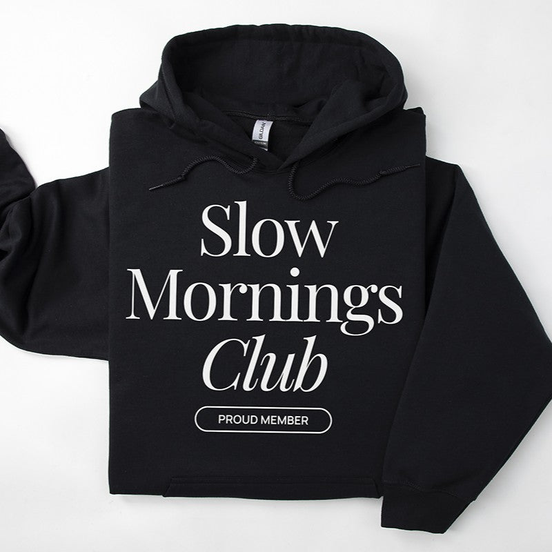 Flatlay of black Slow Mornings Club hoodie featuring cozy coffee-inspired graphic design