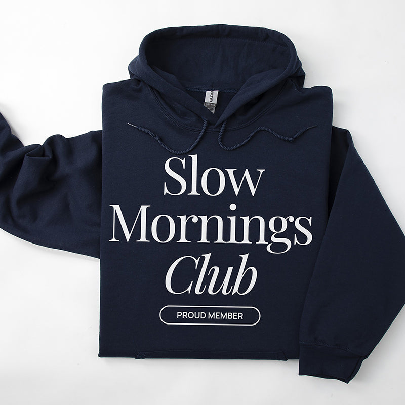 Flatlay of navy Slow Mornings Club hoodie with minimalist slow living graphic