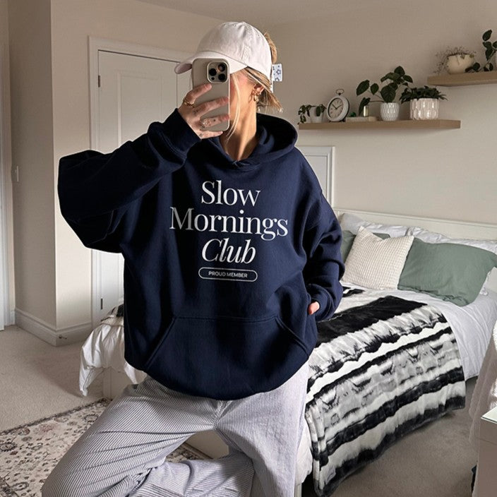 Female model in navy Slow Mornings Club hoodie styled with joggers and a casual hat