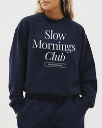 Woman in navy Slow Mornings Club sweatshirt styled with casual bottoms